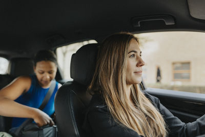 Female blond coach driving while teenage girl sitting behind in car