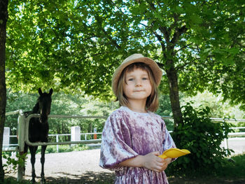 Portrait of small girl wearing lilac dress and summer hat and horse