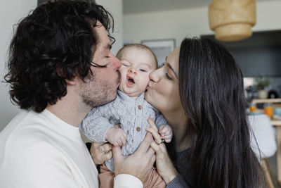 Father and mother kissing baby boy at home