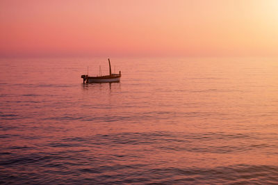 Silhouette boat sailing in sea against orange sky