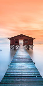 Pier over sea against orange sky