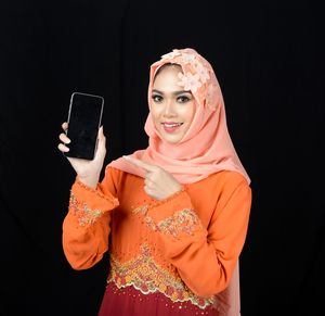 Portrait of smiling woman standing against black background