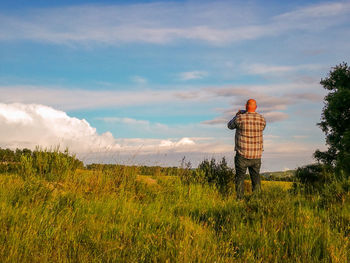 Rear view of man looking at field against sky