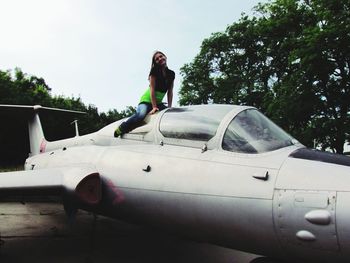 Side view of woman standing on car against sky