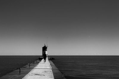 Man walking on jetty against clear sky