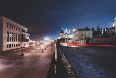 Illuminated buildings by road against sky at night