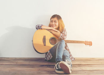 Woman playing guitar against wall