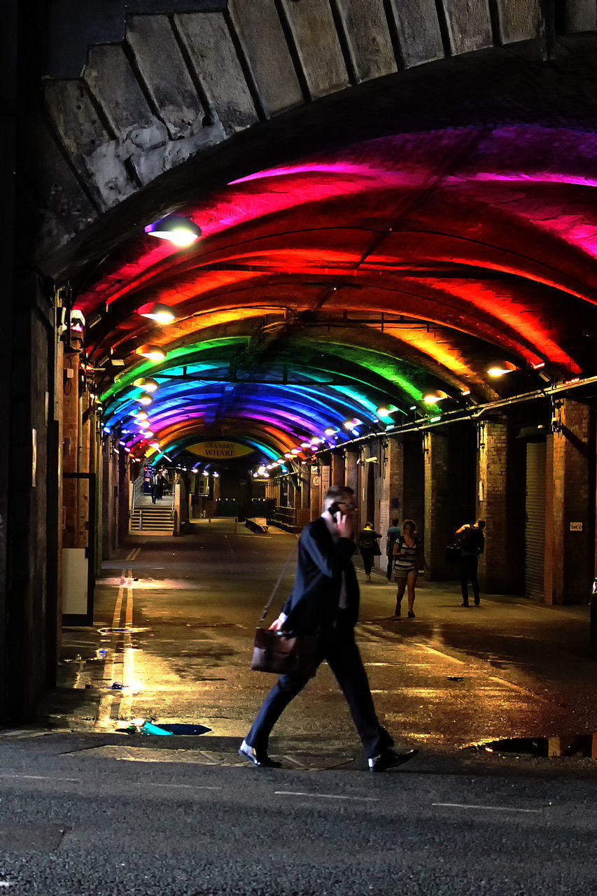 FULL LENGTH OF MAN WALKING AT ILLUMINATED CITY