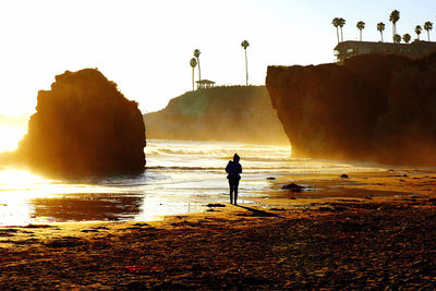 Silhouette man standing on beach against sky during sunset