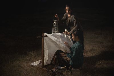 Man holding umbrella while sitting on field at night