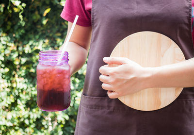 Midsection of woman holding cocktails in jar outdoors
