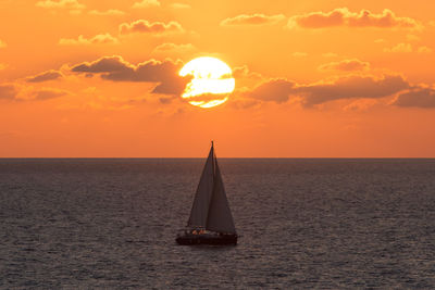 Sailboat sailing on sea against orange sky