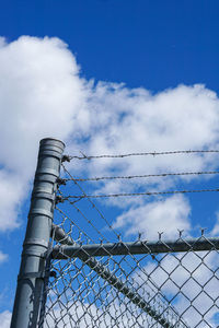 Low angle view of barbed wire fence against blue sky