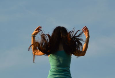 Rear view of young woman with tousled hair against sky
