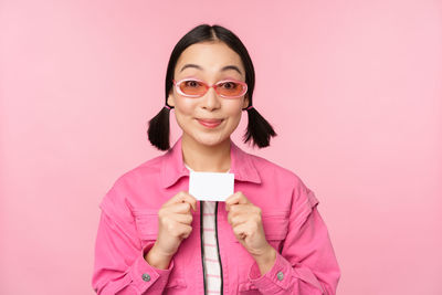 Portrait of smiling young woman against pink background