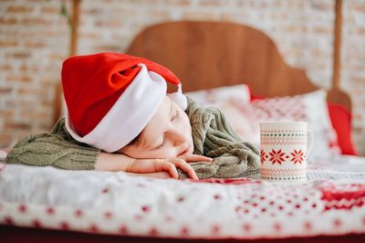 Boy wearing santa hat while sleeping in bed at home