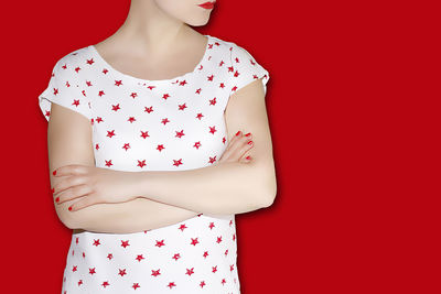 Midsection of woman with arms crossed standing against red background