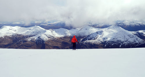 Rear view of person standing on snowcapped mountain against cloudy sky