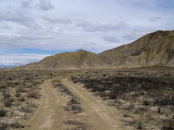 Dirt road on arid landscape against sky