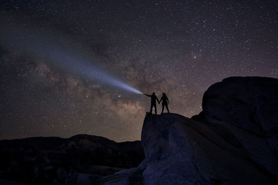 Silhouette people standing on rock against sky at night