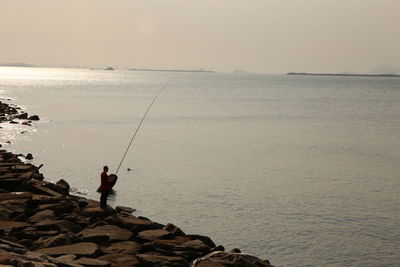 People fishing in sea against sky