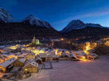 Aerial view of townscape by snow covered mountain against evening sky