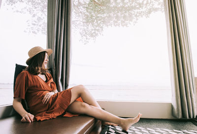 Midsection of woman sitting by window at home