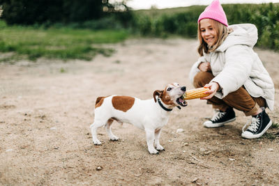 Happy teenage girl hugging and feeding her dog jack russell terrier in a field against the backdrop