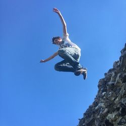 Low angle view of boy jumping from retaining wall against clear blue sky