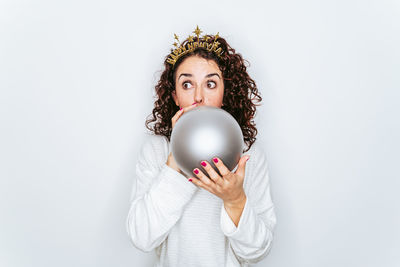 Mid adult woman looking away while blowing balloon against white background