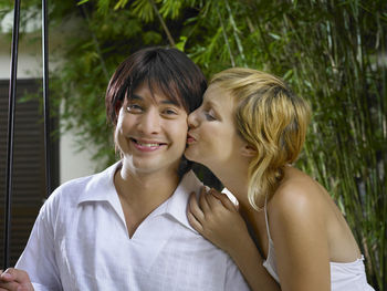 Portrait of smiling boyfriend being kissed by girlfriend while sitting on swing at resort