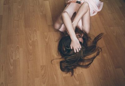 High angle view of depressed woman lying on hardwood floor