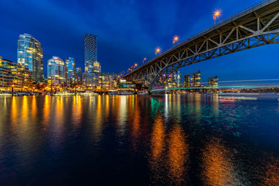 Illuminated bridge over river by buildings against sky at night