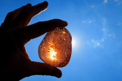 Close-up of hand holding apple against sky