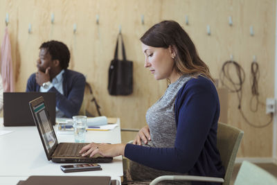 Side view of pregnant businesswoman using laptop at conference table in office