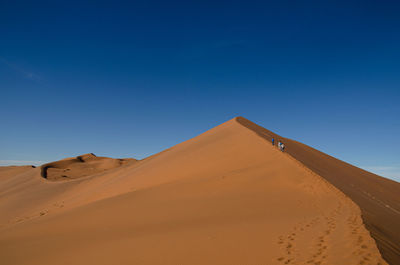 Person walking up orange red sand dune in the middle of the sossuvslei desert region in namibia