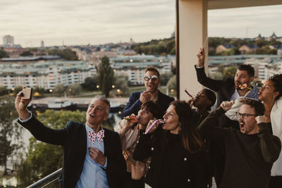 Cheerful male and female colleagues taking selfie on smart phone during party in office