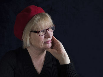 Mature woman with hand on chin against black background