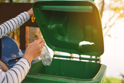 Cropped hands of person throwing bottle in garbage bin