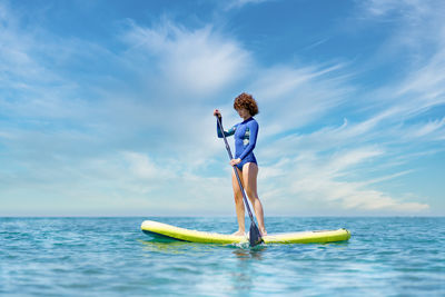 Rear view of woman surfing in sea against sky