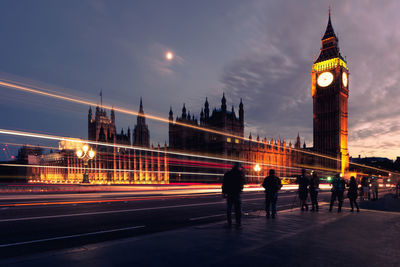 Light trails by big ben on westminster bridge against sky in city at dusk