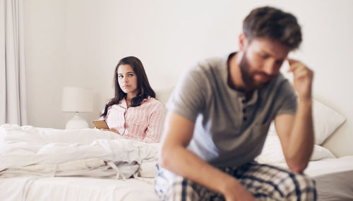 Stressed couple sitting on bed at home