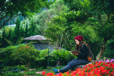 Side view of young woman sitting on plants against trees