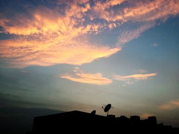 Low angle view of silhouette birds on roof against sky