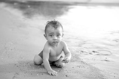 Portrait of cute shirtless baby boy crawling on shore at beach