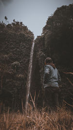 Rear view of man standing on field looking at waterfall