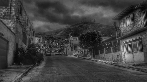 Empty road amidst houses against storm clouds