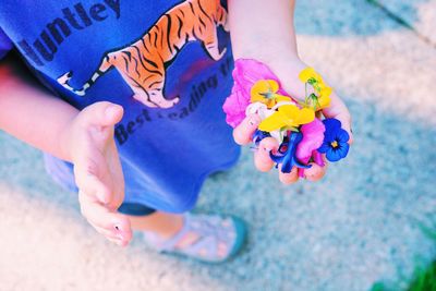 Low section of child holding colorful flowers on footpath