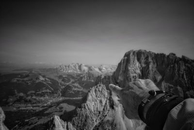 Close-up of man pointing at mountain against sky