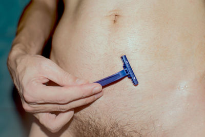 Midsection of shirtless man shaving abdomen